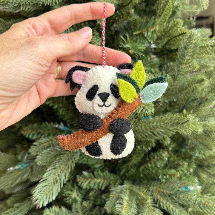 Hand holding a panda ornament with leaves against a Christmas tree background