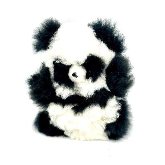 A plush toy resembling a panda with black and white fur, made from recycled alpaca fur, handcrafted in Peru.