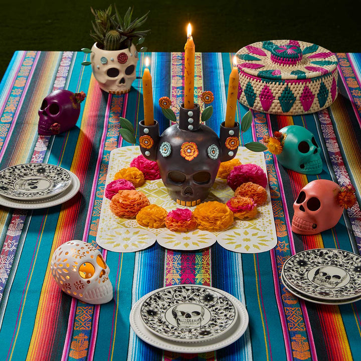 Decorative setup with skull-shaped candles, colorful skulls, and a striped tablecloth.