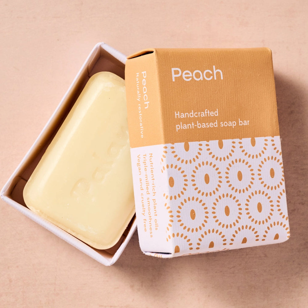 Handcrafted plant-based peach soap bar with packaging on a beige background
