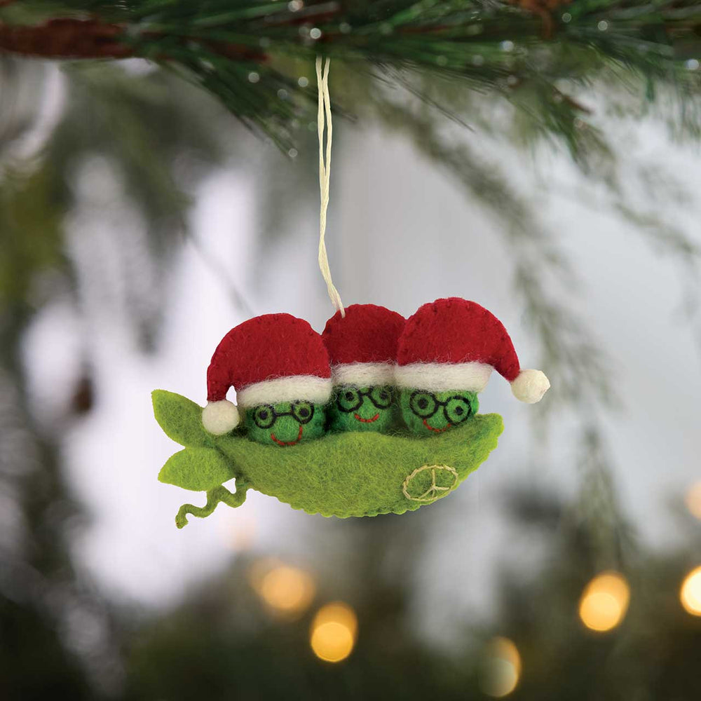 Christmas ornament with three green peas wearing red hats hanging from a tree branch.