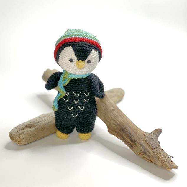 Knitted penguin toy with a colorful hat and scarf on a wooden branch against a white background