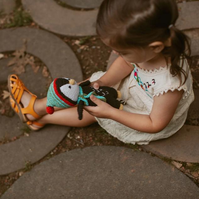 Child holding a knitted penguin toy on a stone path