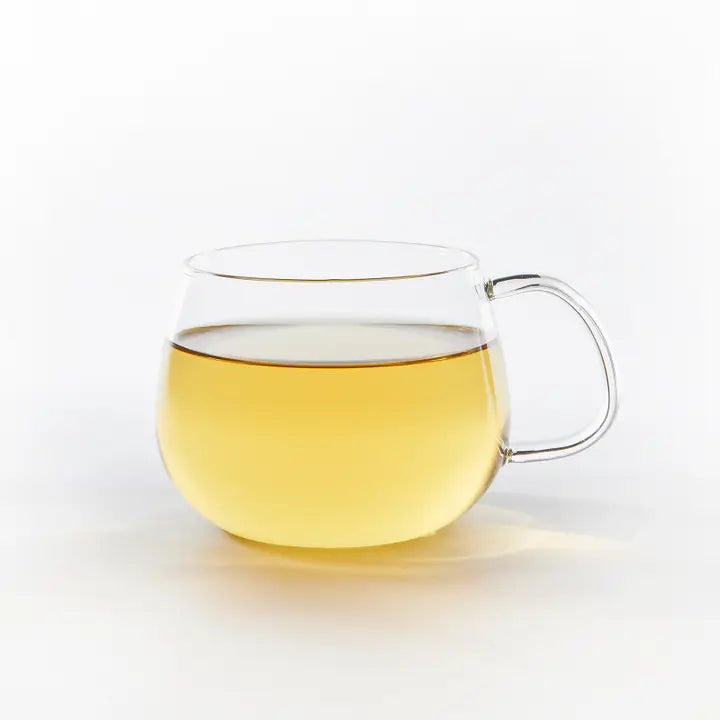 Clear glass mug with handle filled with yellow  tea on a white background