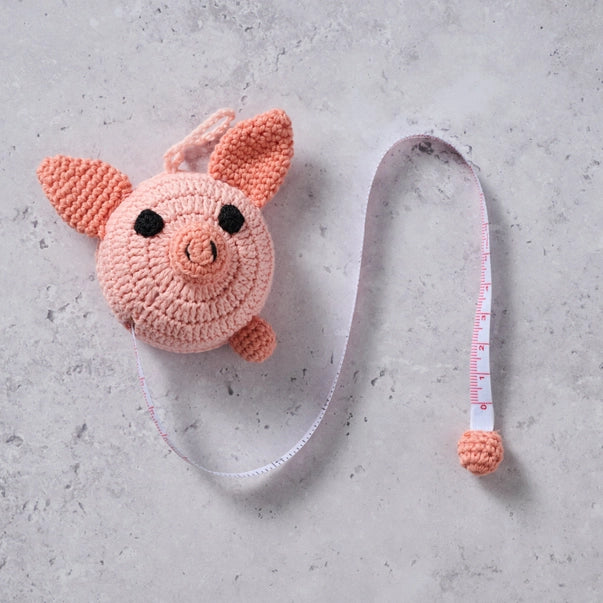 Crocheted pig-shaped measuring tape on a gray surface