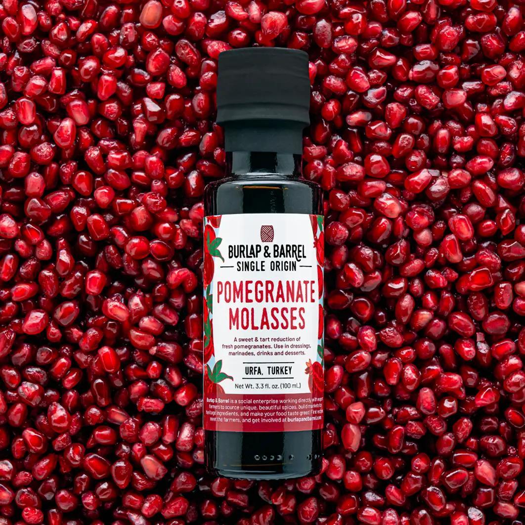 Burlap & Barrel Pomegranate Molasses bottle on a background of pomegranate seeds