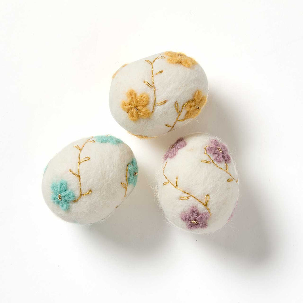 Three embroidered felt eggs with floral designs on a white background