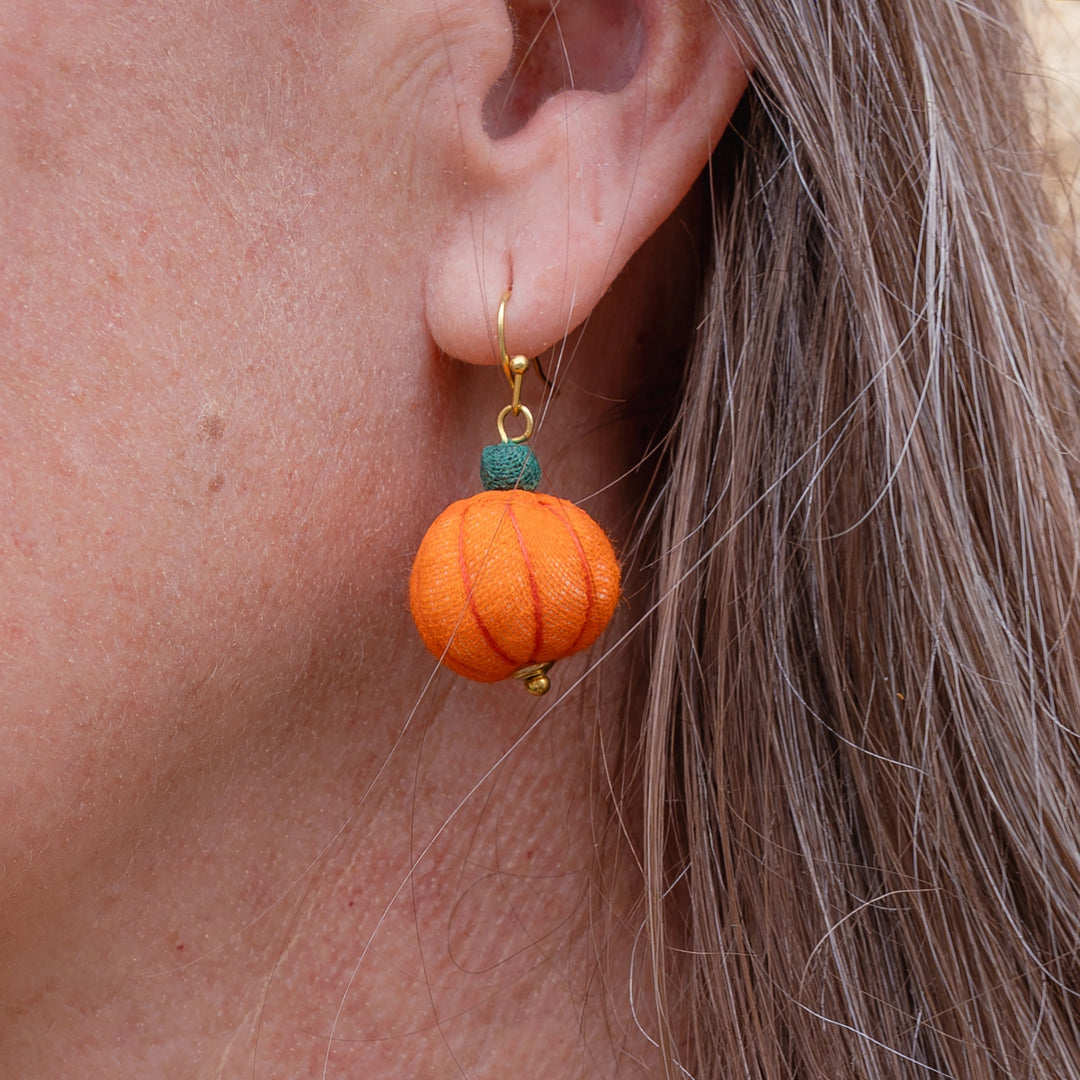 Close-up of pumpkin-shaped earring worn by a person.
