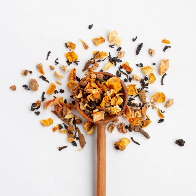 Wooden spoon filled with pumpkin spice tea leaves on a white background