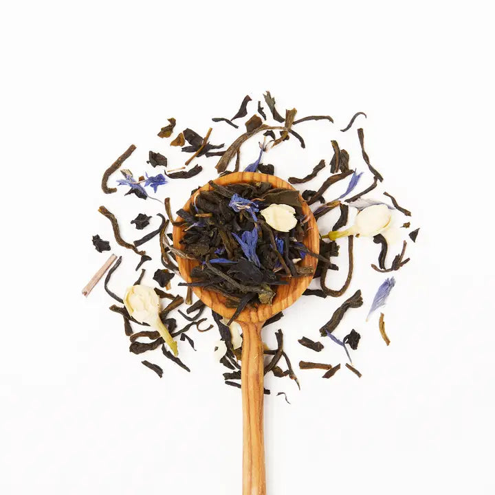 Wooden spoon filled with assorted tea leaves on a white background