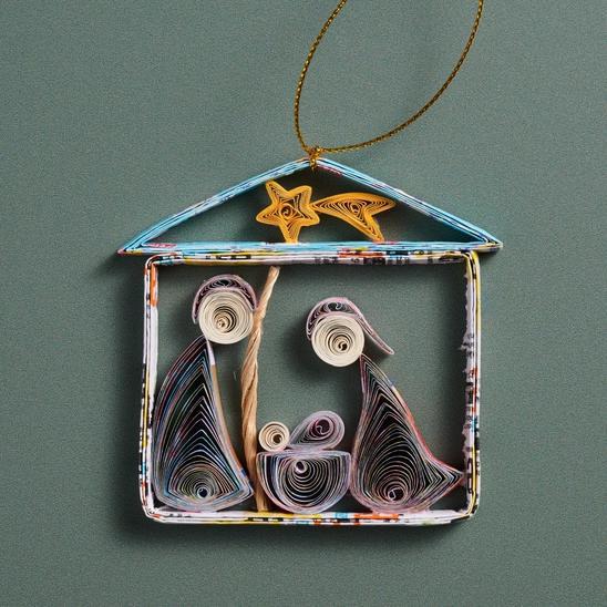 A handmade quilled nativity ornament featuring the figures of the nativity scene within a rectangular frame, adorned with colorful, intricate designs and a golden hanger at the top.