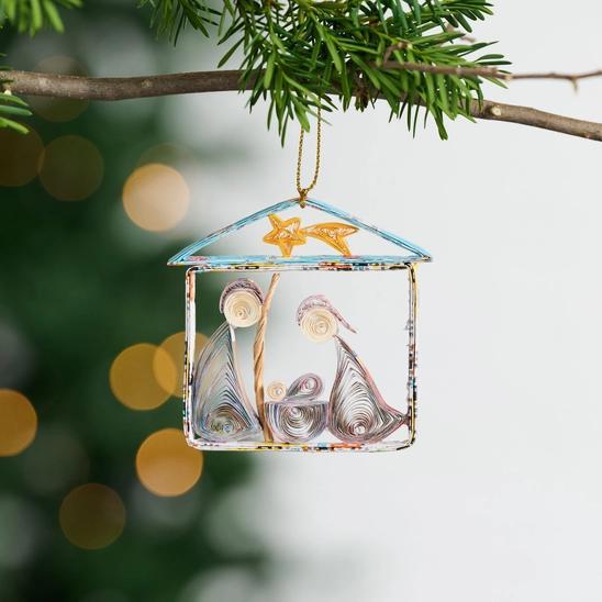 A handmade quilled nativity ornament featuring the figures of the nativity scene within a rectangular frame, adorned with colorful, intricate designs and a golden hanger at the top.