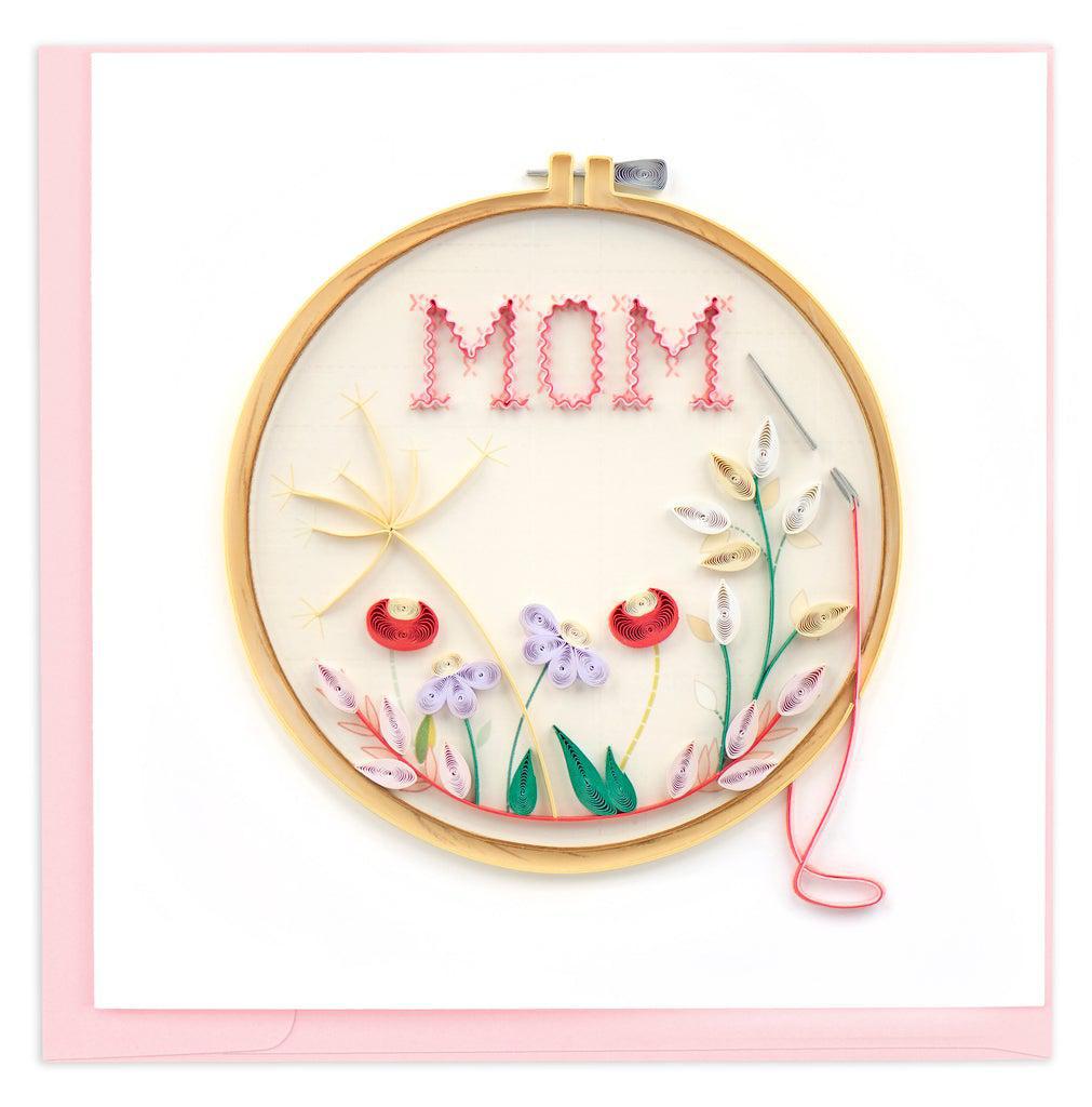 A quilled card with a circular design featuring the word 'MOM' in the center, surrounded by a floral pattern.