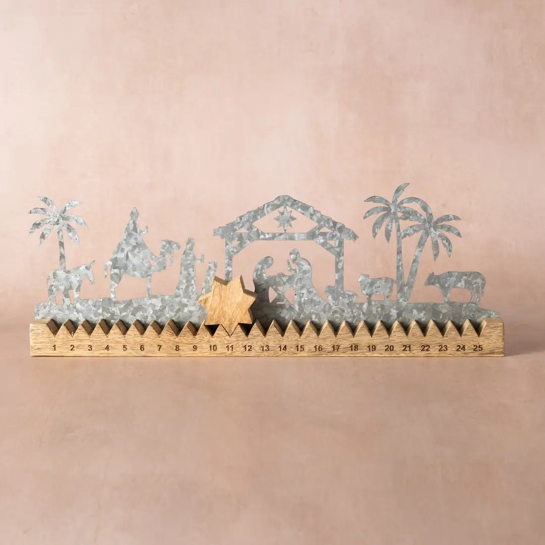 Galvanized metal nativity scene silhouette decoration with a wooden ruler base showing countdown to Christmas, set against a solid beige background.