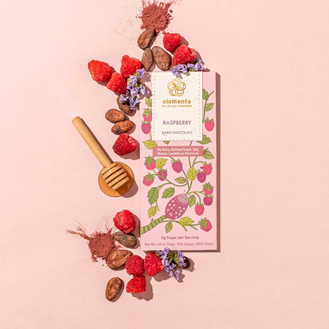 Raspberry dark chocolate bar with raspberries, cocoa powder, and a honey dipper on a pink background