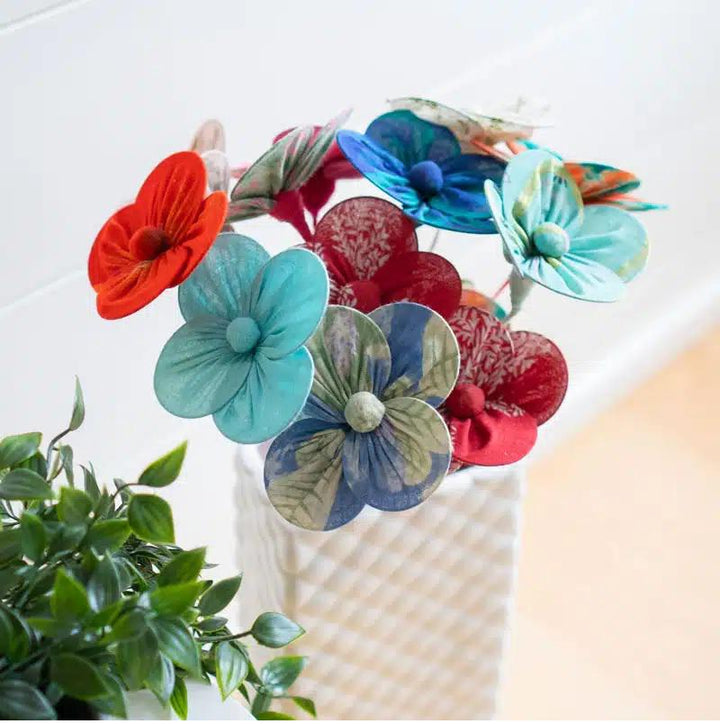 A collection of handmade flowers from recycled sari fabric in a variety of colors displayed in a white milk vase.