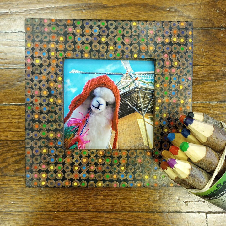 Colorful pencil frame with a photo of a llama wearing a red hat on a wooden surface.