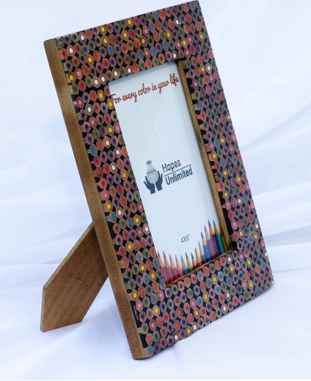 A handmade picture frame constructed from recycled colored pencils, designed to fit a 4x6 photo, with a wooden stand and glass cover.
