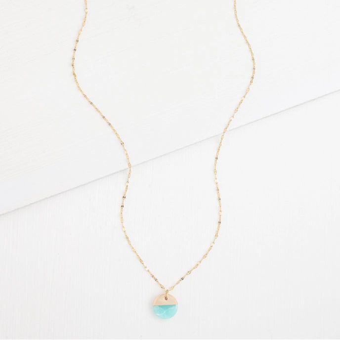 A gold necklace with a round aqua pendant on a white stone background