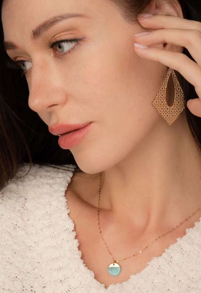 A woman wearing a aqua pendant on a gold chain.