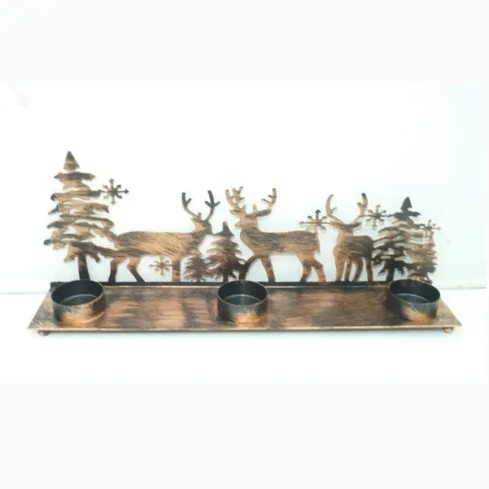 A rustic metal holiday candle holder featuring three deer, pine trees, and snowflakes in a distressed bronze finish, with three small cup holders along the bottom, set against a plain white background.