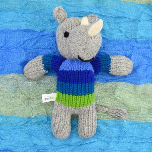Knitted rhino toy animal wearing a blue and green sweater on a blue fabric background
