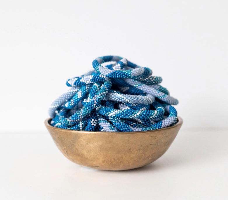 Beaded roll-on bracelets with various blue patterns and shades in a display bowl.
