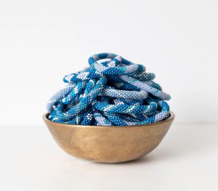 Beaded roll-on bracelets with various blue patterns and shades in a display bowl.