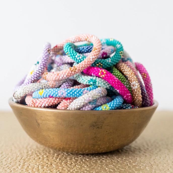 Beaded roll-on bracelets with many colors and a flower design displayed in a bowl.