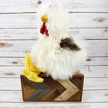 A plush toy depicting a rooster made from alpaca fur, displayed on a wooden structure with a geometric pattern.
