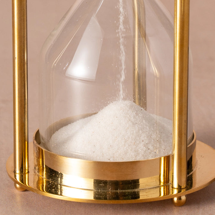 Gold hourglass with sand running through on a beige background
