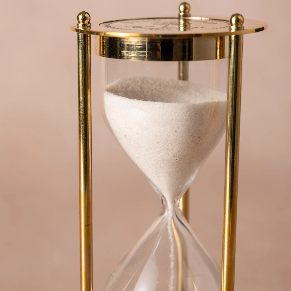 Gold hourglass with sand on a pink background
