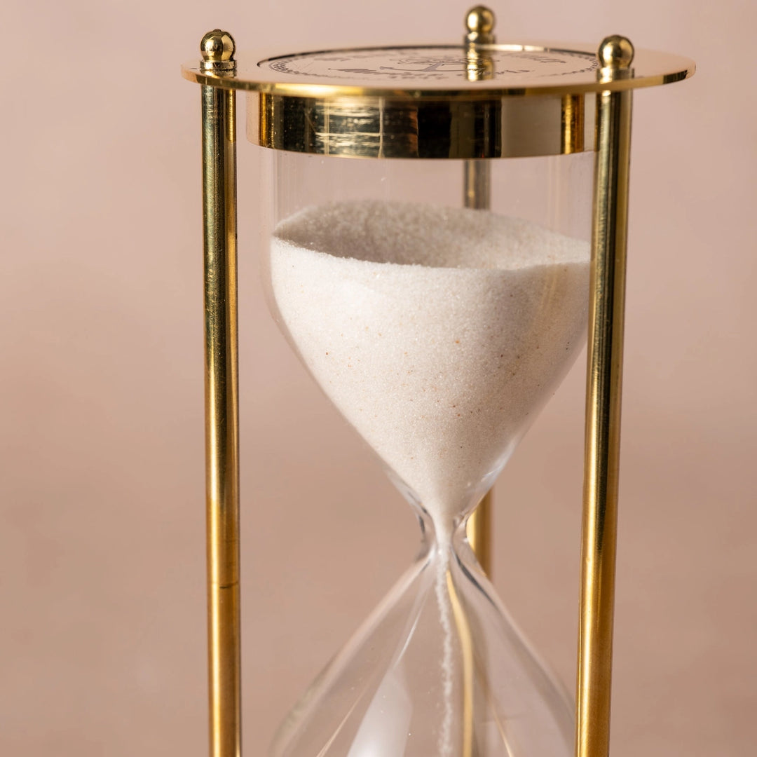 Gold hourglass with sand on a pink background