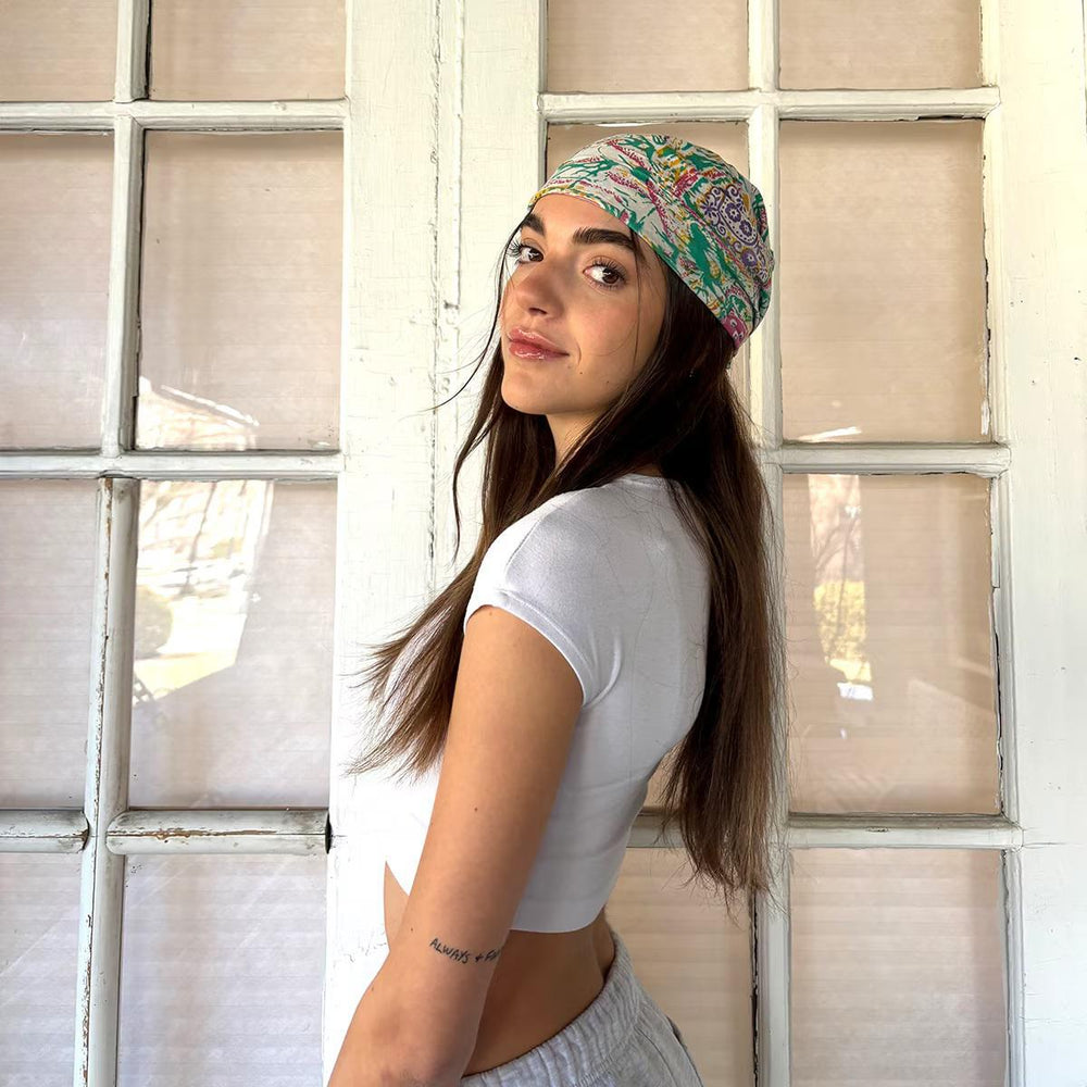 Woman wearing a colorful bandana and white crop top in front of a window.