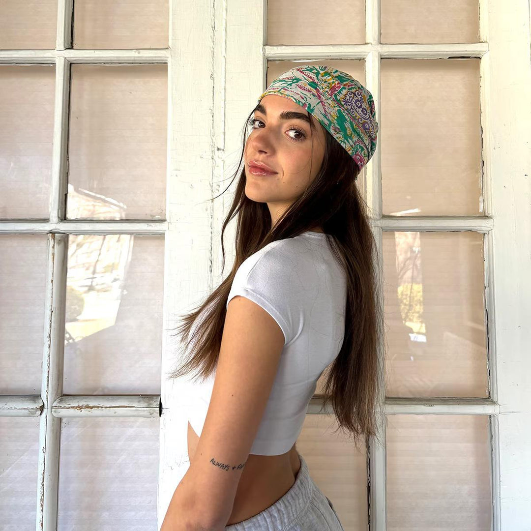 Woman wearing a colorful bandana and white crop top in front of a window.