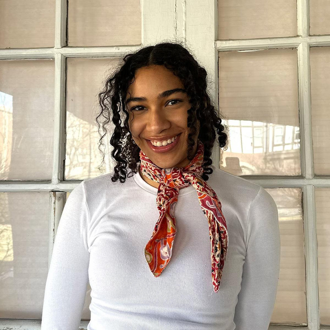 Woman wearing a white shirt and colorful bandana in front of a glass paneled wall.