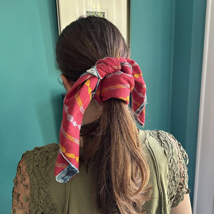 Person with a red patterned bandana tied in a ponytail against a teal wall.