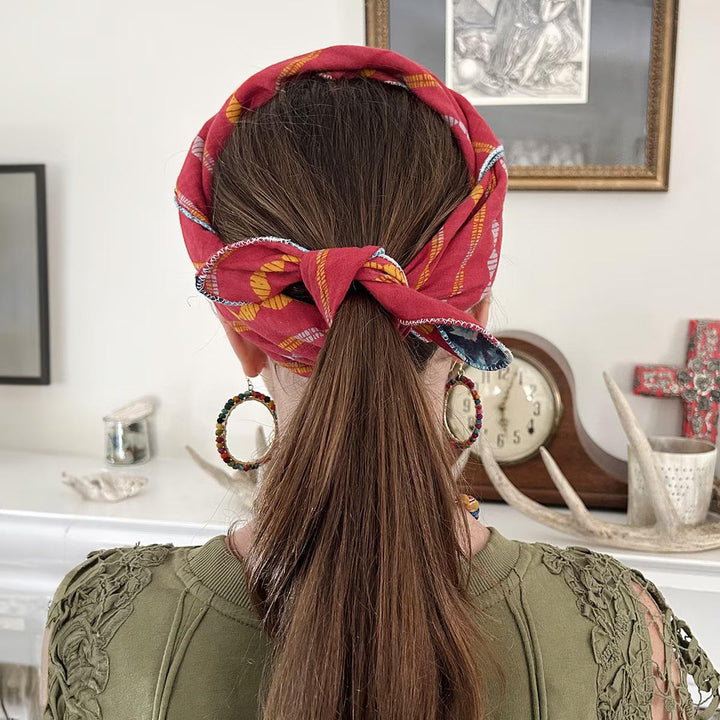 Person with a red patterned bandana and earrings in an indoor setting