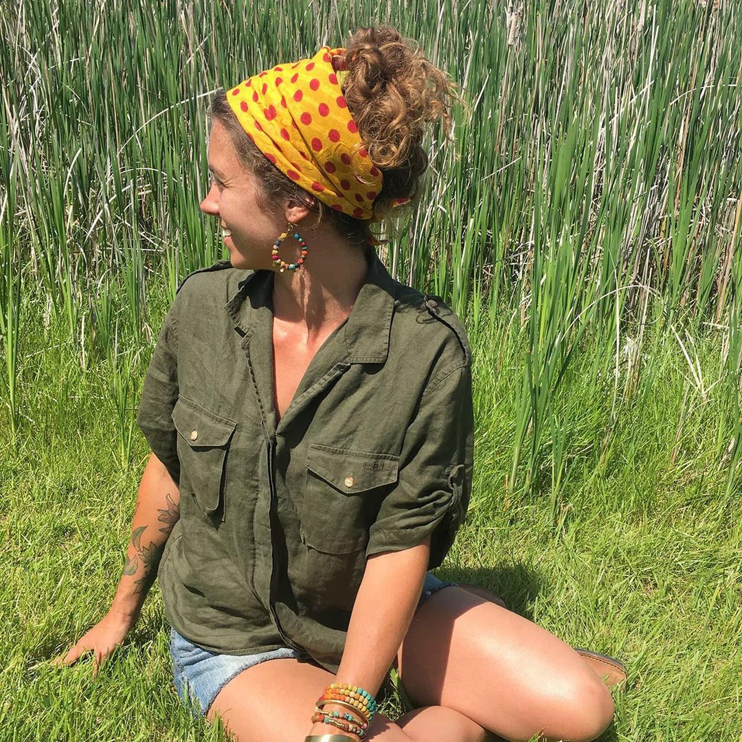 Woman sitting in tall grass wearing a yellow polka dot bandana.