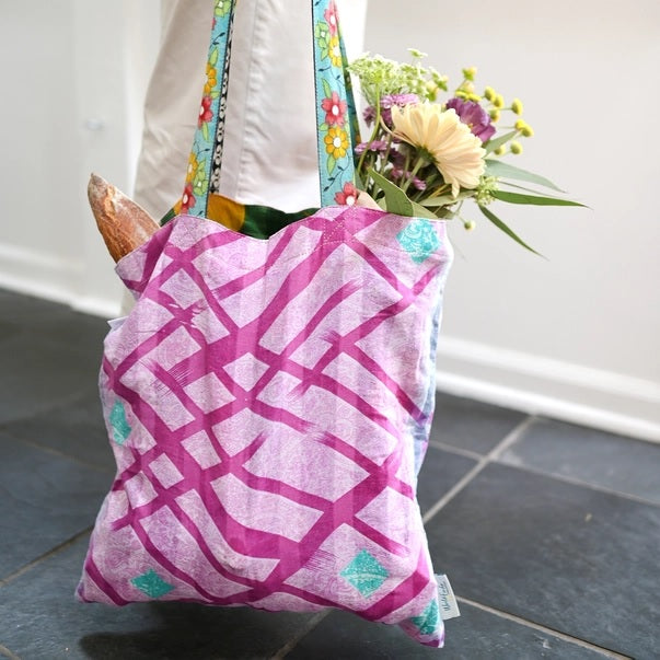 sari tote bag with pink geometric pattern held by a person with flowers and bread.