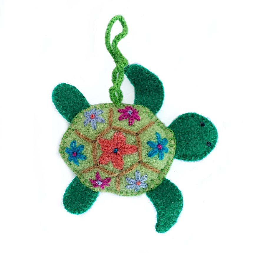 A handmade felt turtle ornament with a green body, a light green shell decorated with colorful embroidered flowers, and a green hanging loop at the top, shown on a plain white background.
