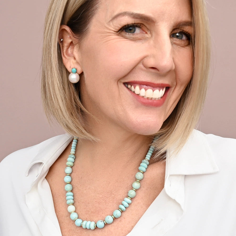 Woman wearing a white shirt and turquoise necklace against a beige background