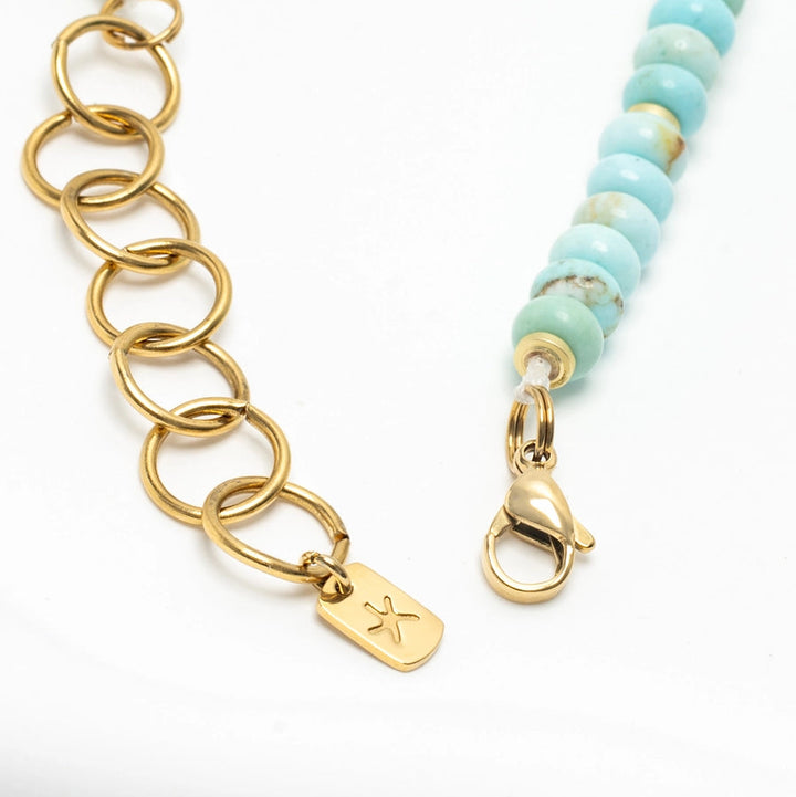 Gold chain necklace with a tag and turquoise beaded necklace on a white background