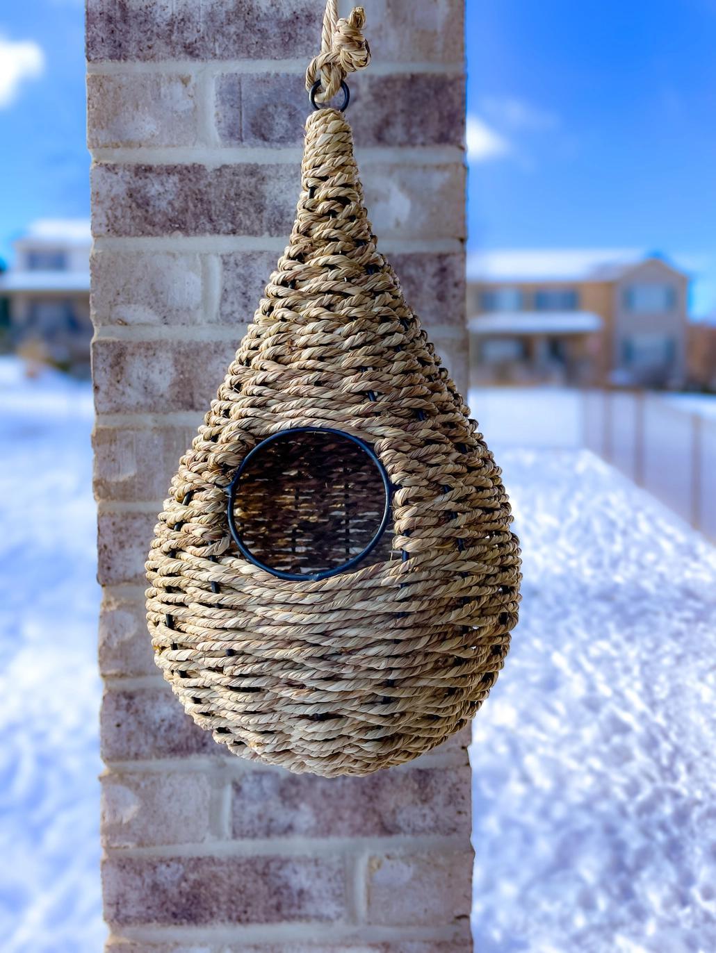 A teardrop-shaped birdhouse made of natural seagrass, with a visible metal framework inside, hanging from a loop at the top.