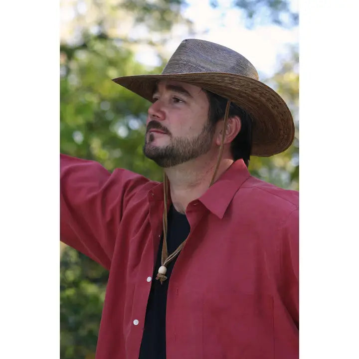 Man wearing a straw hat and red shirt outdoors with greenery in the background