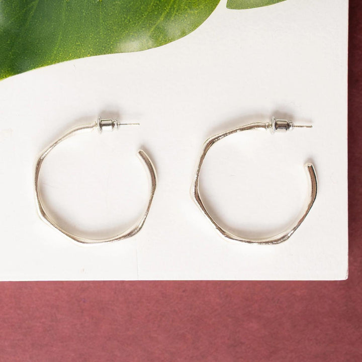 Silver hexagonal hoop earrings on a white surface with a green leaf