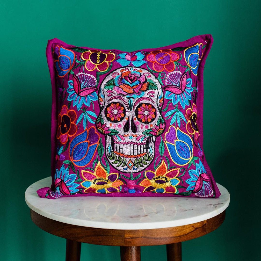 Colorful skull and floral patterned pillow on a small round table against a green background