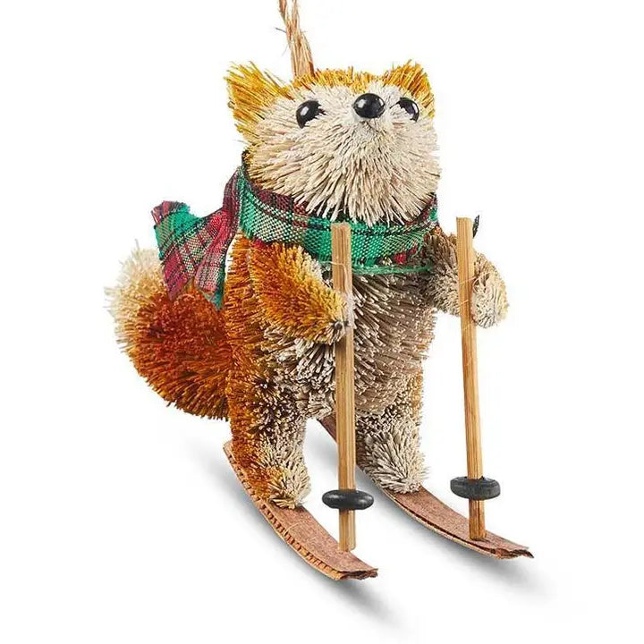 A small buri animal ornament shaped like a brown and cream fox wearing a green plaid scarf, with wooden ski poles and skis, photographed on a white background.
