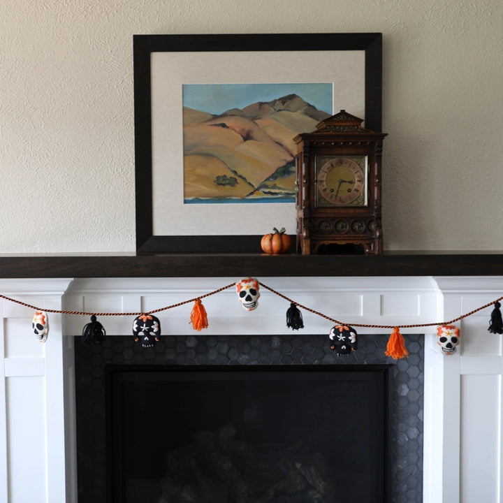 Decorative Halloween garland on a fireplace mantel with a clock and framed picture in the background.