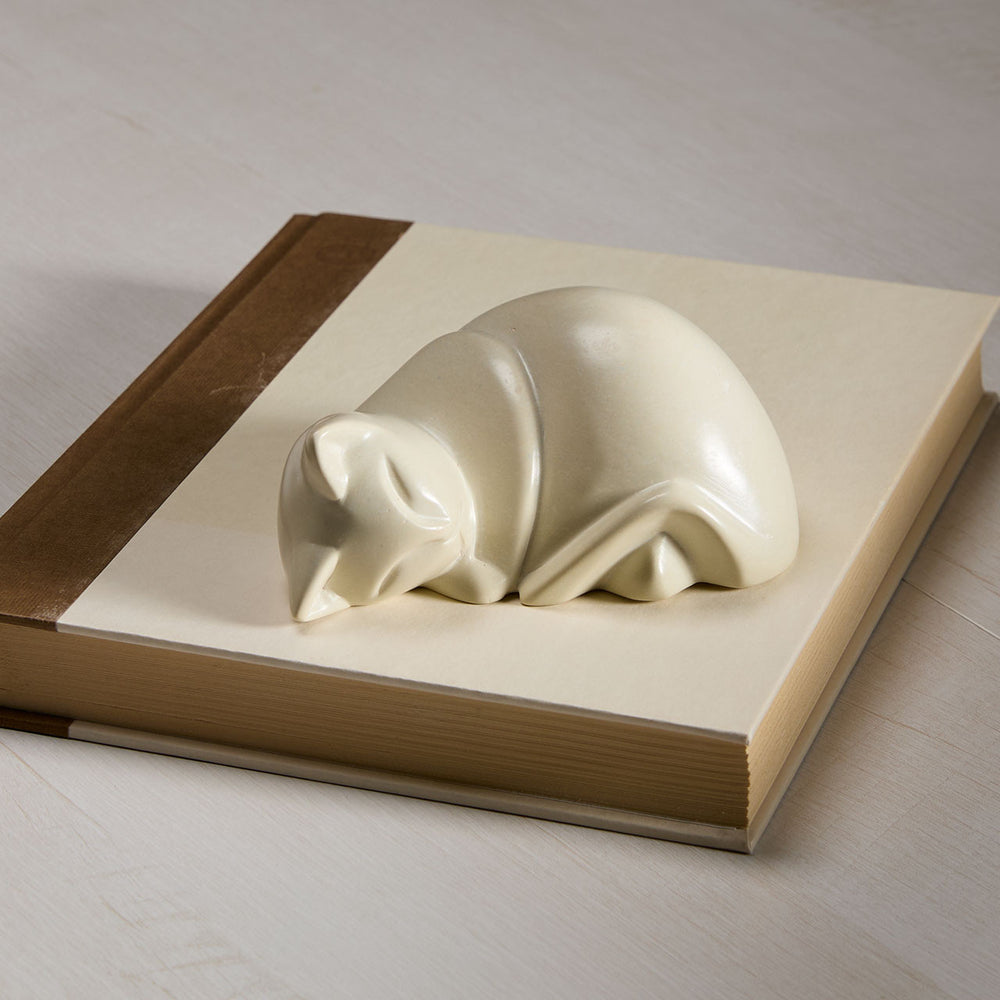 cream soapstone cat figurine on an open book with a wooden cover.